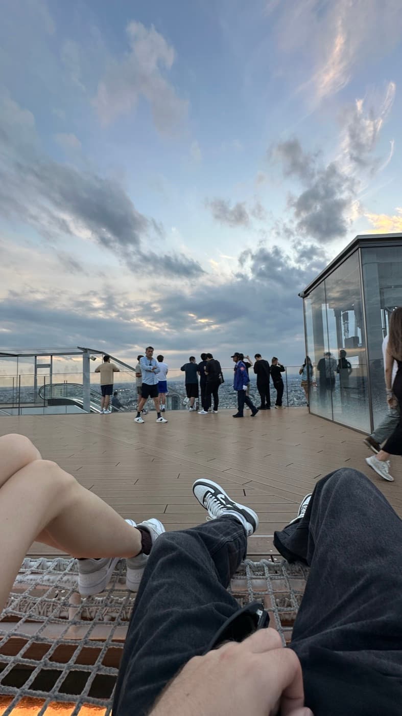 Blick aus einer Netzhängematte auf dem Rooftop, im Hintergrund andere Besucher und Wolkenhimmel