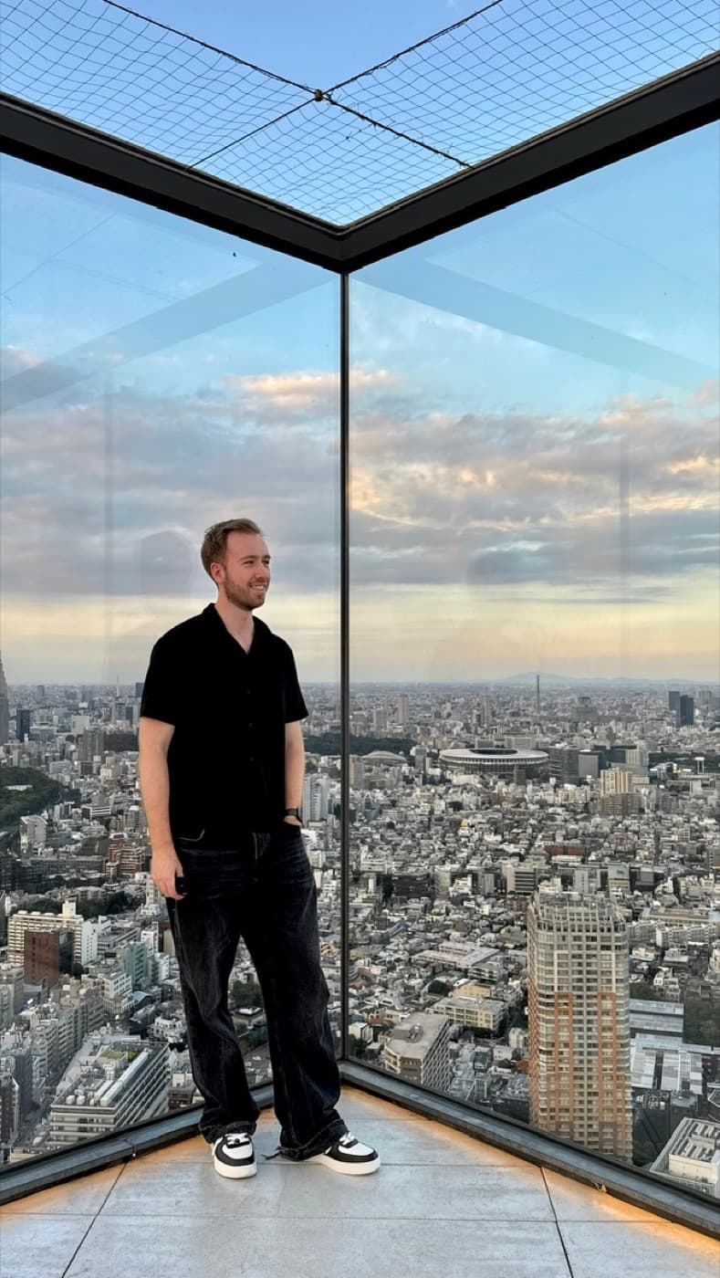 Person an der verglasten Ecke des offenen Rooftops von Shibuya Sky in der Dämmerung